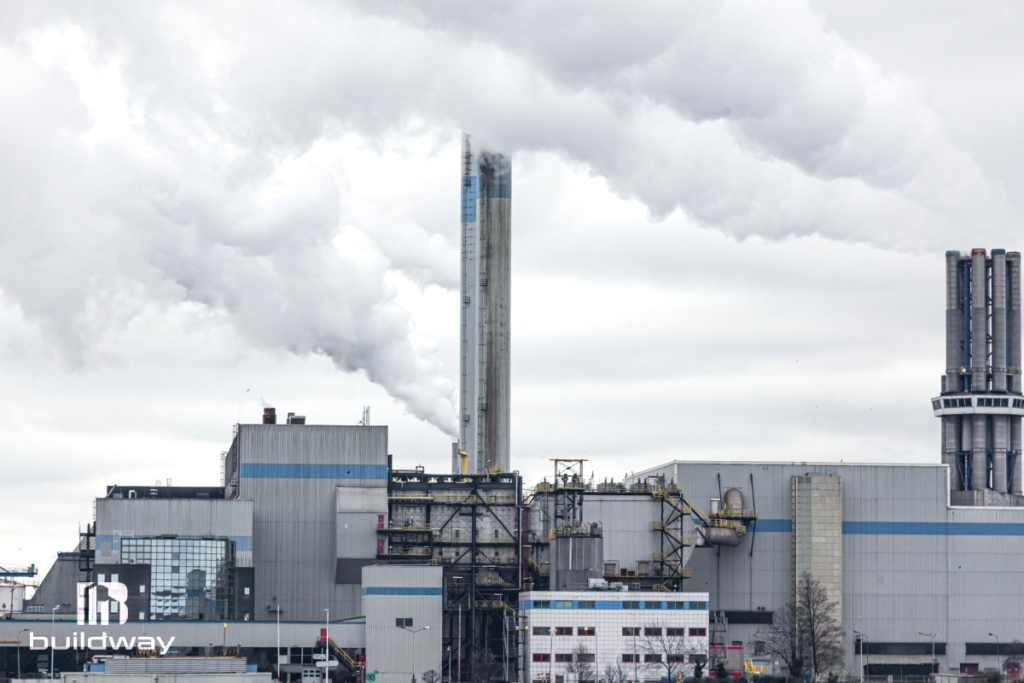 Large industrial manufacturing plant with metal structures and tall chimneys emitting steam, showcasing Buildway’s durable construction design.