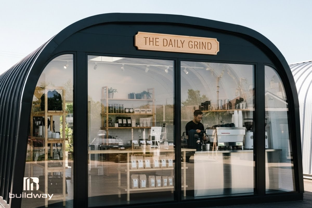 Modern Quonset-style coffee shop named ‘The Daily Grind’ with large glass windows and sleek black metal framing, showcasing Buildway’s contemporary retail building design.