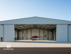 Large steel aircraft hangar, featuring wide sliding doors and a red helicopter inside. Designed for commercial aviation use with durable construction and spacious interior.
