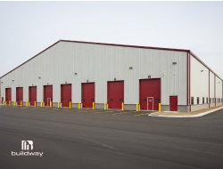 Large industrial steel warehouse with multiple red roll-up doors and a durable metal exterior, constructed by Buildway. Ideal for commercial storage, logistics, and manufacturing operations.