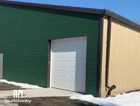 Green I-beam metal building with white downspout and garage door, showcasing Buildway’s water drainage accessories.