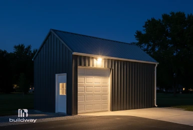 Compact custom steel garage with a single roll-up door and side entry, illuminated at night, designed for simplicity, functionality, and long-term reliability.