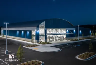 Modern steel sports facility with a curved roof and glass entrance, illuminated at night, built to meet local codes for safety, functionality, and long-term durability.
