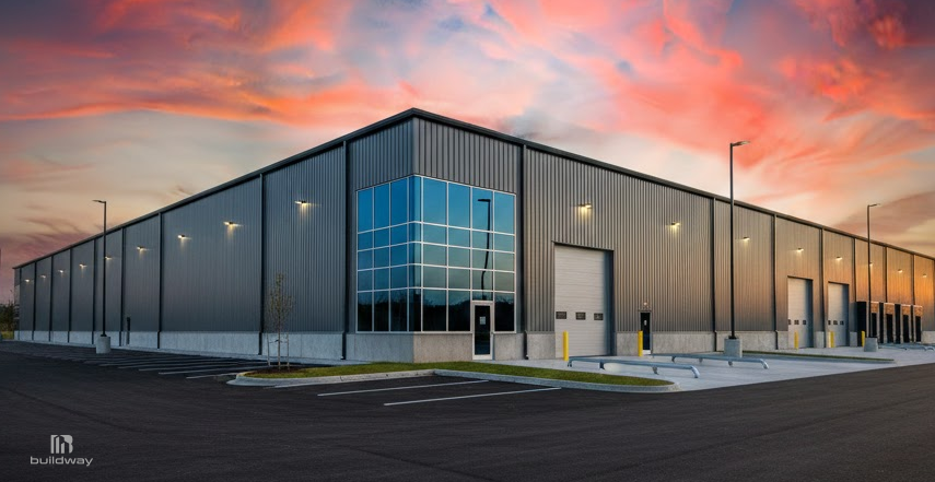 How Long Do Steel Buildings Last If You Ignore Maintenance? The Result Is Brutal 1 Modern steel warehouse with metal siding, large glass windows, and multiple loading bay doors, set in a clean industrial lot at sunset.