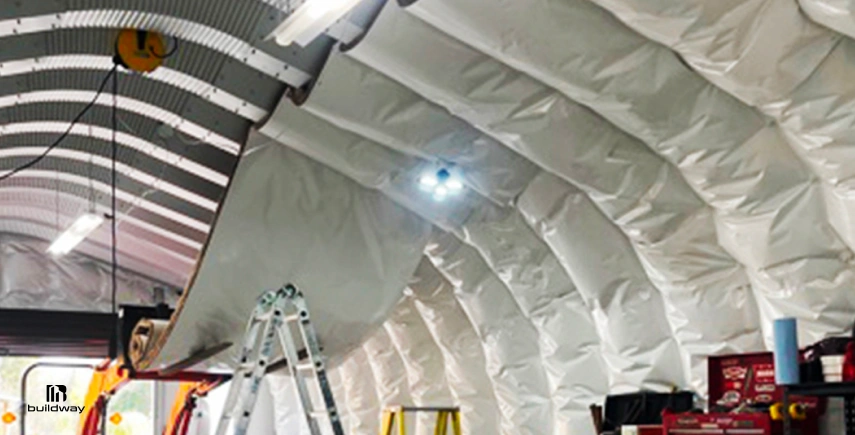How to Personalize a Steel Building Without Wasting Money on the Wrong Parts 7 Interior of a Quonset-style steel building with white insulation panels being installed along the curved ceiling structure.