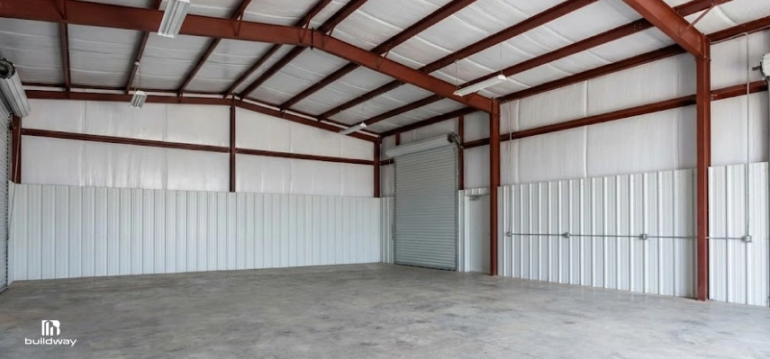 How to Personalize a Steel Building Without Wasting Money on the Wrong Parts 8 Interior of a steel building featuring red steel framing, insulated white walls, metal liner panels, and a roll-up garage door.